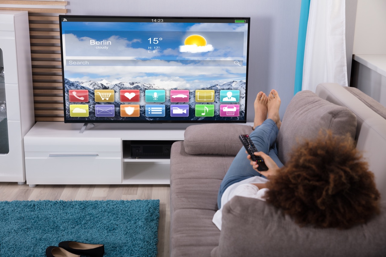 Frau auf dem Sofa vor einem Smart TV mit Apps auf dem Bildschirm